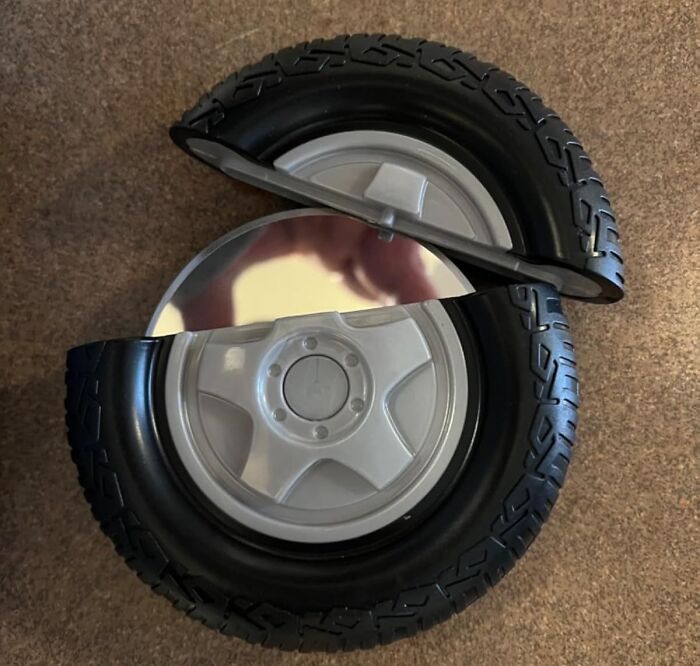 Round black wheel with reflective surface, creatively folded in half, on a textured brown carpet.