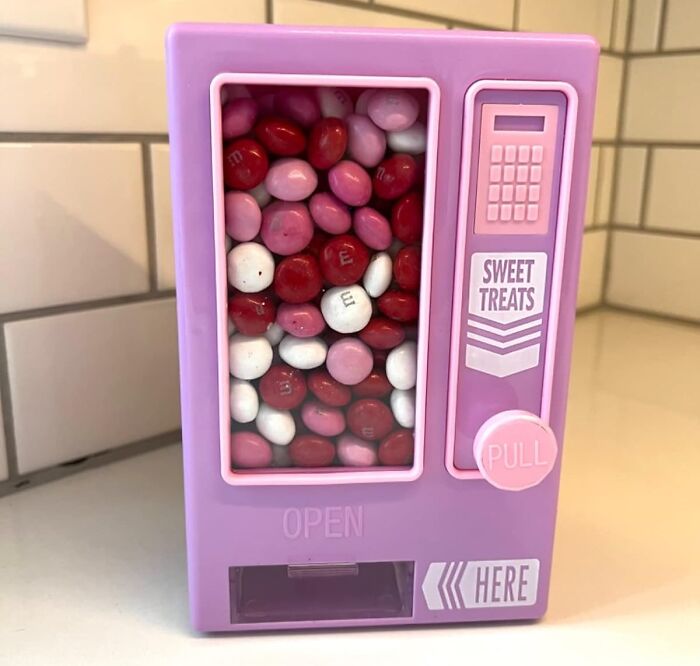 Purple candy dispenser labeled "Sweet Treats," filled with pink, red, and white M&M's.