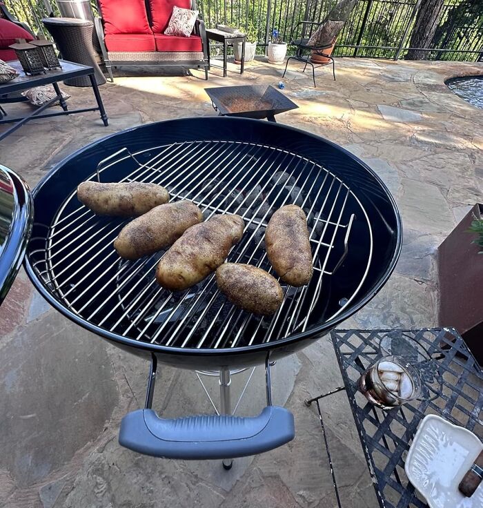 Charcoal grill with potatoes, part of backyard dreams spring must-haves, set on a stone patio.