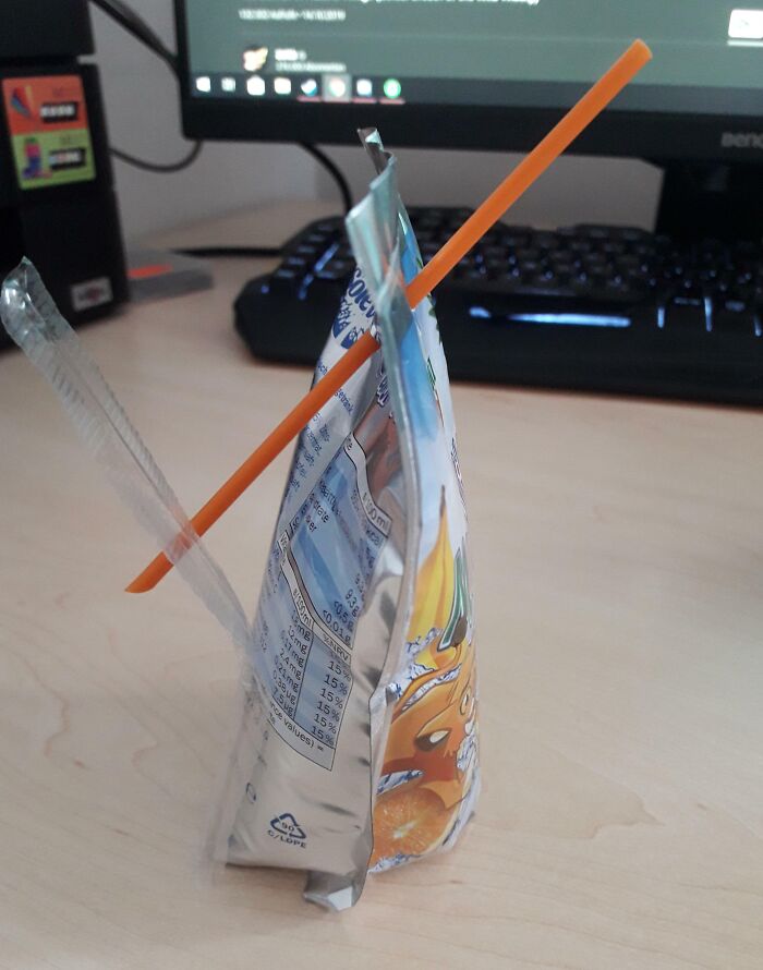 "Error al insertar un popote de bebida en un empaque sobre un escritorio junto a una computadora."