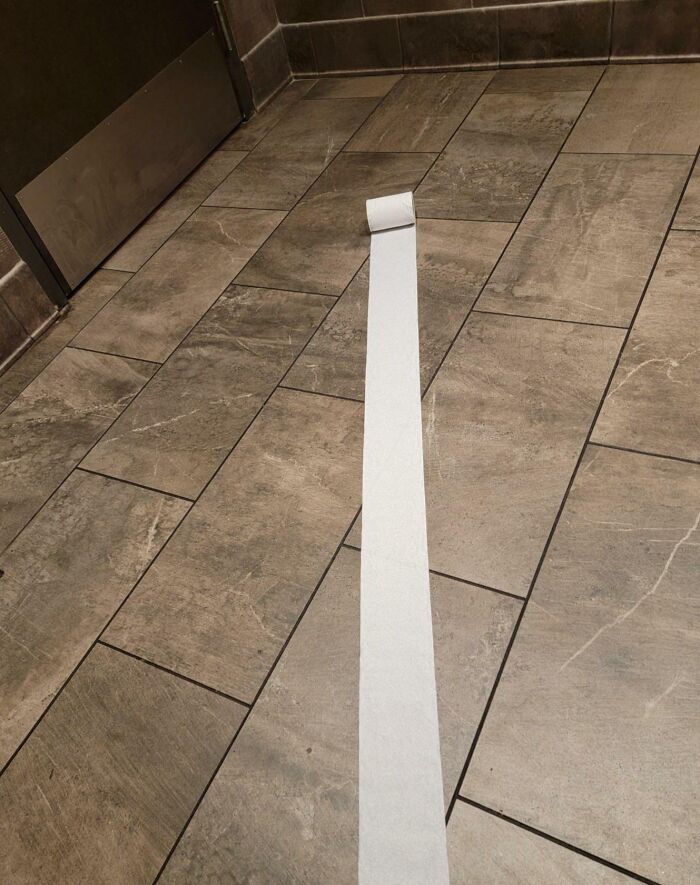A long strip of toilet paper unrolled across a tiled bathroom floor, suggesting a worse day scenario.