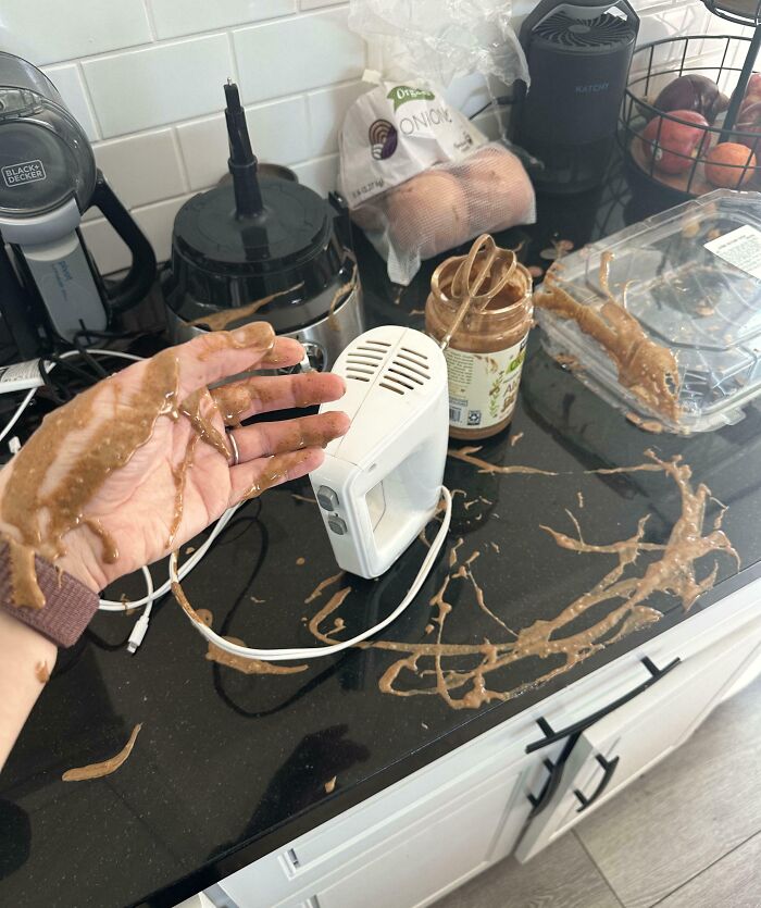 Messy peanut butter spill with a mixer and spread over countertop and hand, illustrating a bad day.
