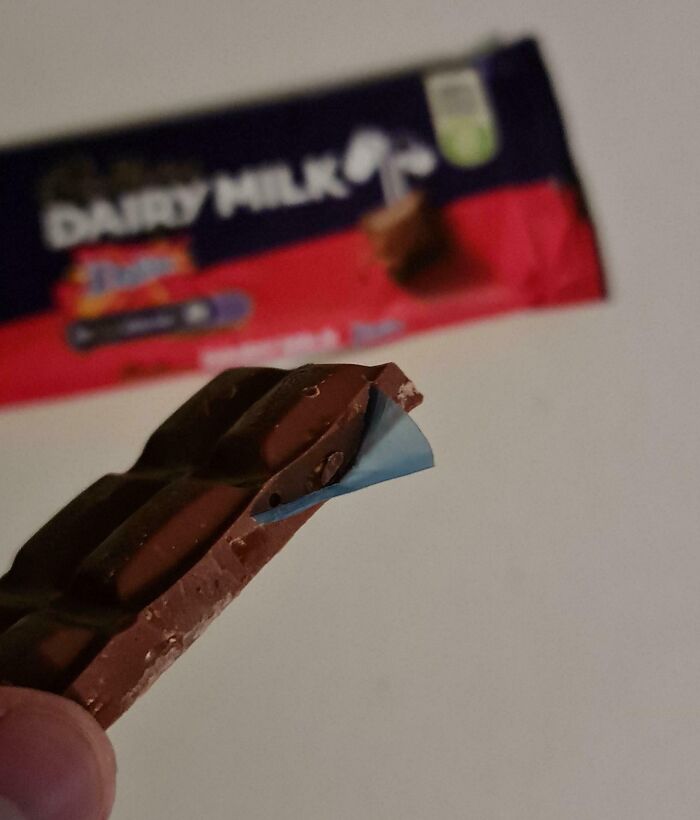 Chocolate bar with a piece of blue plastic embedded, revealing something disgusting while trying to enjoy food.