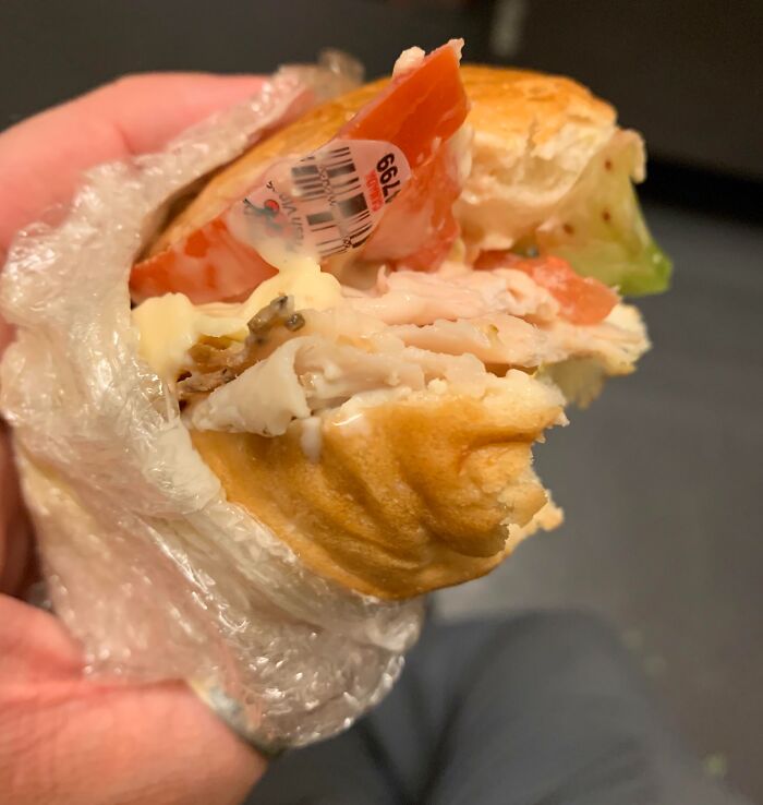 Sandwich with a tomato slice featuring a price sticker, wrapped in plastic, highlighting a food-related surprise.