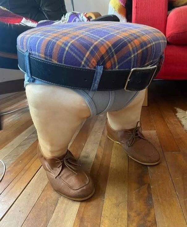 Strange thrifted item resembling legs in shoes, with a plaid seat cushion top and belt, on a wooden floor.