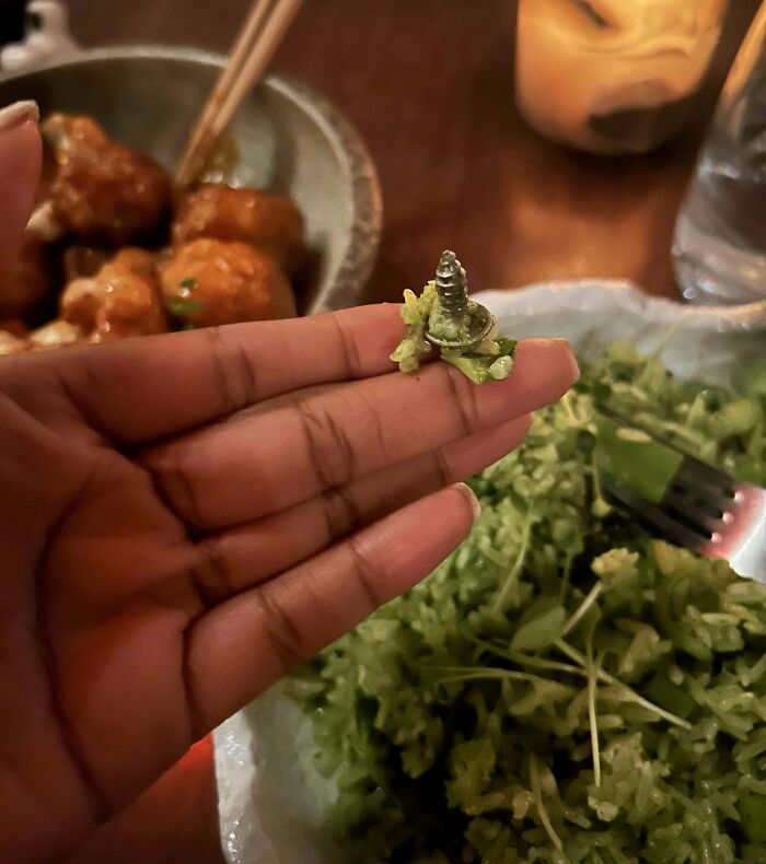 Hand holding a salad with a s***w inside, highlighting a disgusting food discovery.