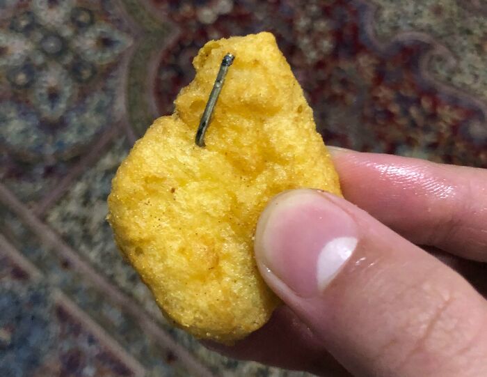 Disgusting food find: A chicken nugget with a metal nail embedded in it, held between fingers.