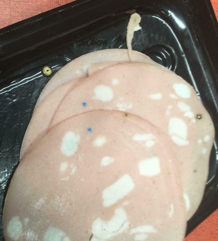 Slices of deli meat with a stringy object, unexpectedly found in food, creating a disgusted reaction.