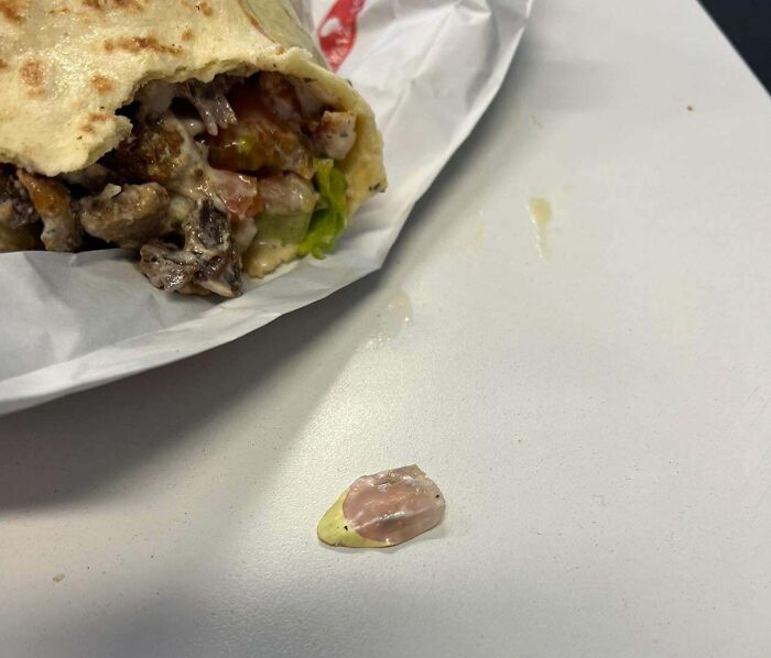 Disgusting find in wrap: a nail on the table beside a partly eaten sandwich, wrapped in paper.