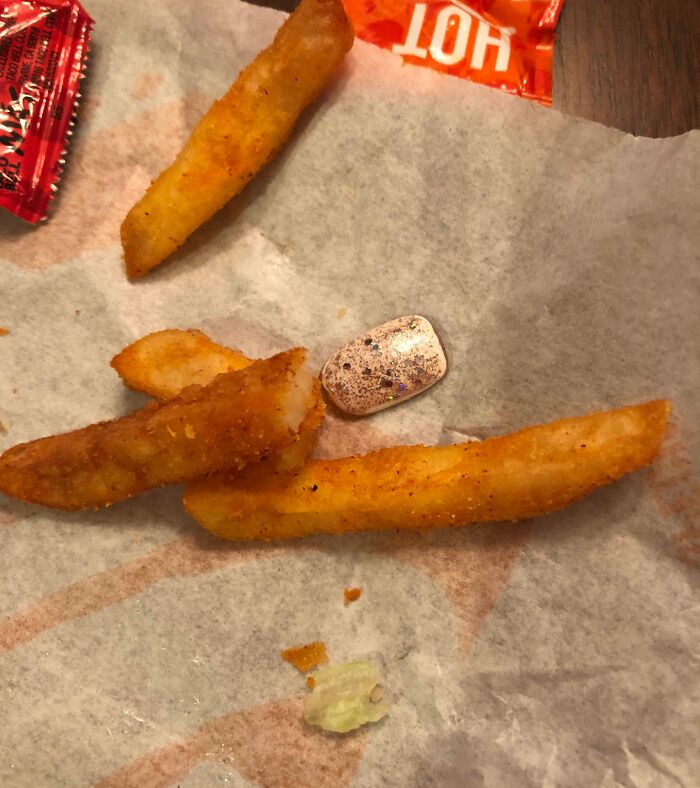 Disgusting surprise in food: French fries with a fake nail on a paper napkin.
