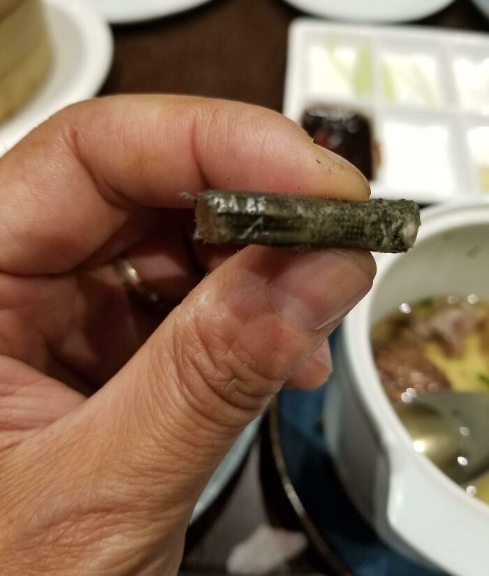 Hand holding a slice of dark, unappetizing food item found while dining.