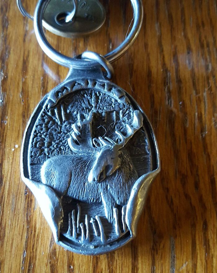 Llavero metálico antiguo con diseño de ciervo, mostrando signos de desgaste por el tiempo sobre mesa de madera.