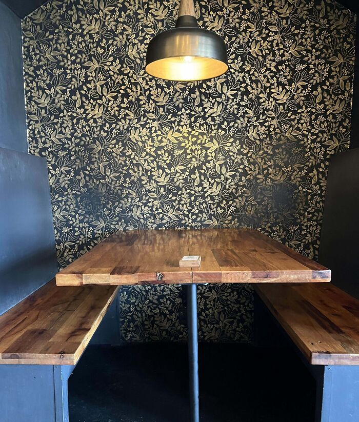 Worn-down wooden table with benches beneath a floral patterned wall and a hanging lamp above.