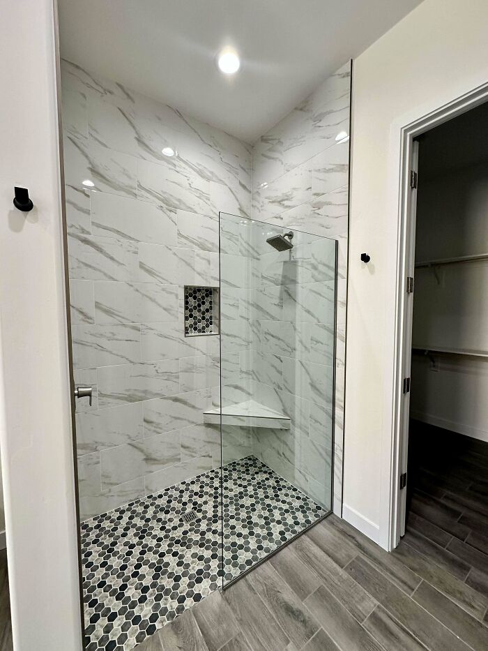 Modern bathroom shower with glass partition and patterned floor showing poorly-aging interior design trends to avoid.