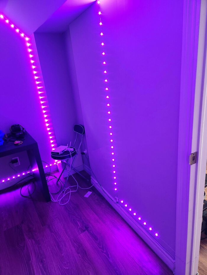 Purple LED strip lighting installed along the walls in a corner of a room with wooden flooring and cables visible.