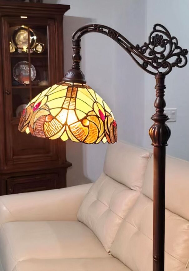Antique stained glass lamp with intricate design found while thrifting, positioned beside a white leather sofa.