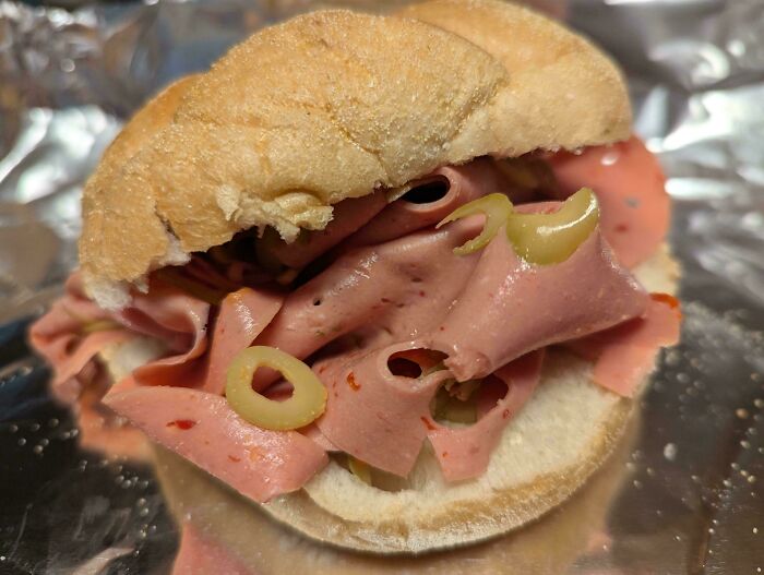 Sandwich filled with old-school delicacy, featuring sliced meat and olives on a bun.