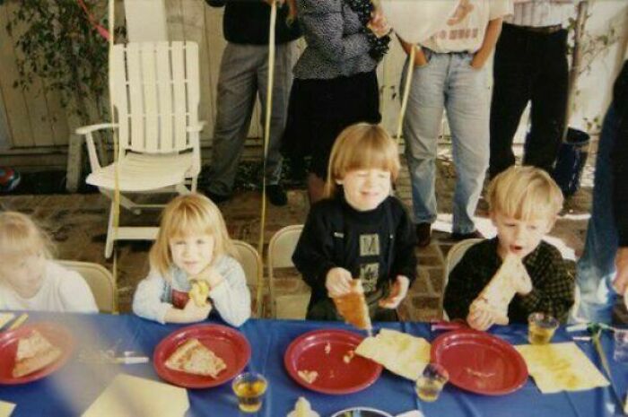 Children enjoying pizza at a party, smiling and having fun around a table with paper plates and drinks.