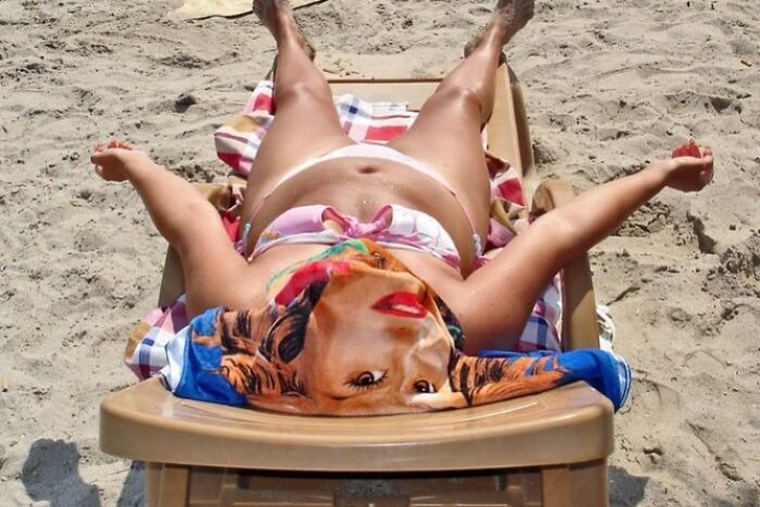 Person lounging on a beach chair with a towel depicting a face, creating a perfectly timed street photo illusion.