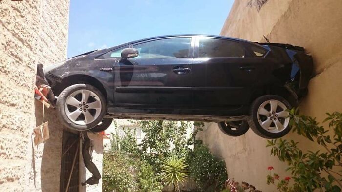 Car stuck between two walls, seemingly defying gravity, in an unusual photography moment.