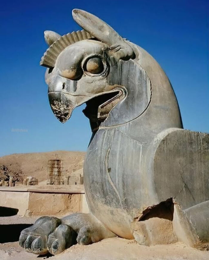 Ancient civilization sculpture of a mythical creature with a beak, large eyes, and wings, set against a clear blue sky.