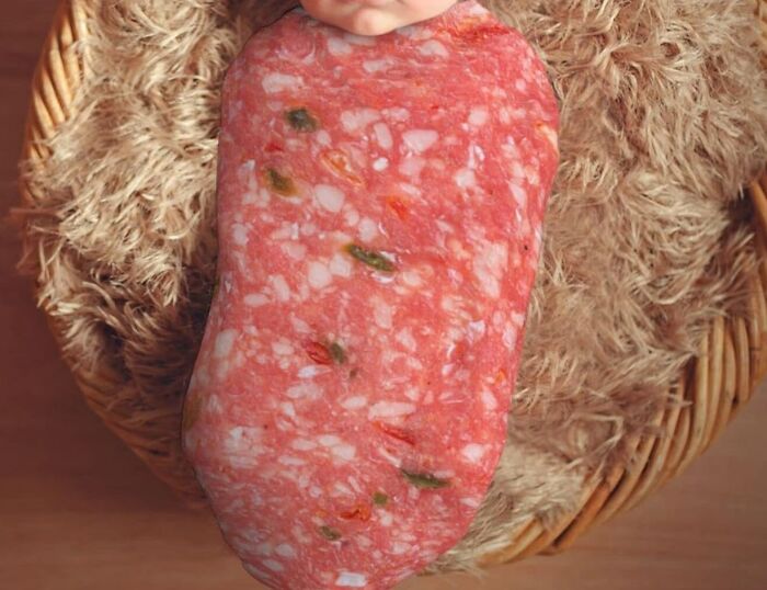 Close-up of a patterned baby blanket resembling salami, wrapped around an infant in a basket.
