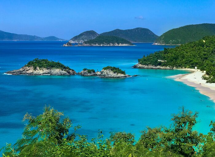 Stunning beach with turquoise waters, lush greenery, and distant islands under a clear blue sky.