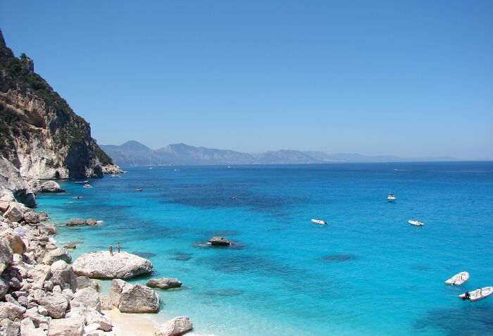 Stunning beach with clear blue water, rocky shoreline, and small boats, ideal for travel inspiration.