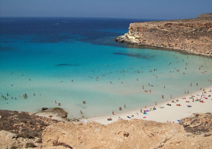 Stunning beach with turquoise waters and sunbathers, surrounded by rocky cliffs.