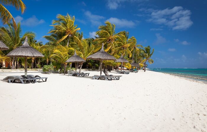 Stunning beach with white sand, palm trees, and straw umbrellas under a clear blue sky.