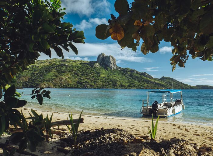 A stunning beach with clear waters, a docked boat, and lush green hills in the background.