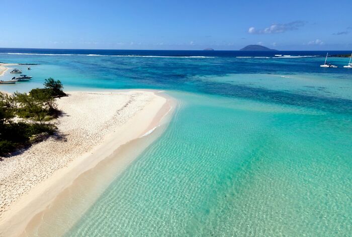 Stunning beach with turquoise water and white sand, bordered by lush greenery, under a clear blue sky.