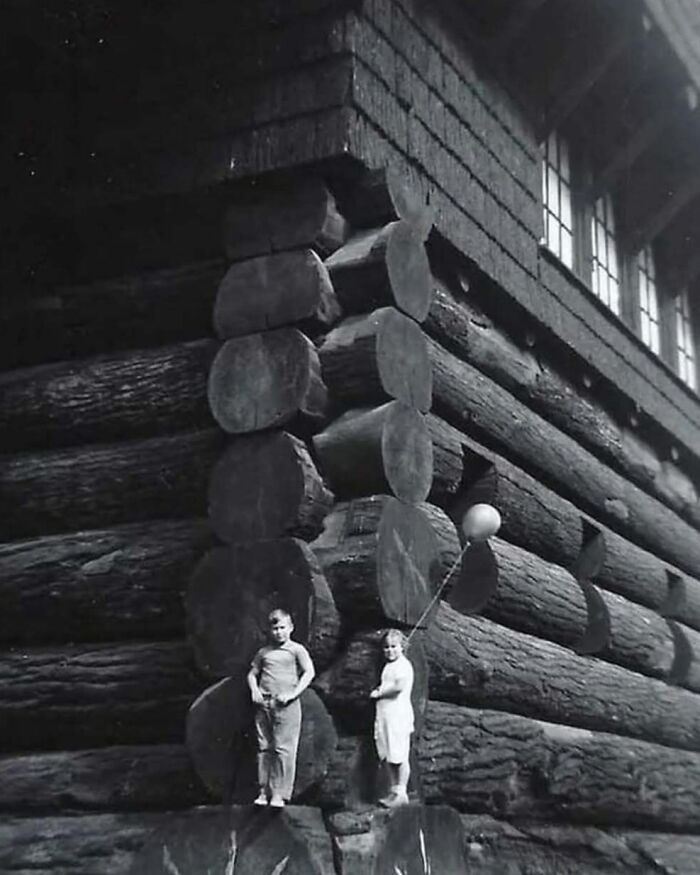 Children standing by a large log cabin showcasing unique American architecture.