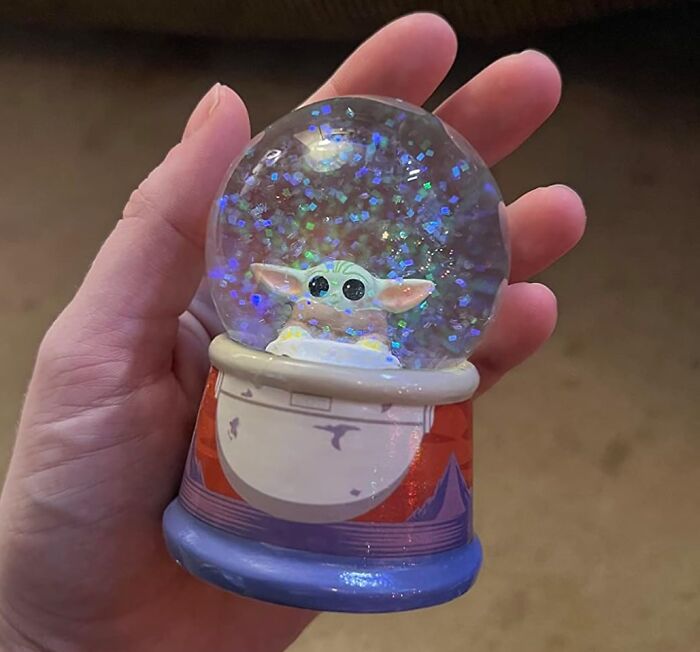 Hand holding a Baby Yoda snow globe, capturing pure fandom goals with glittering details.