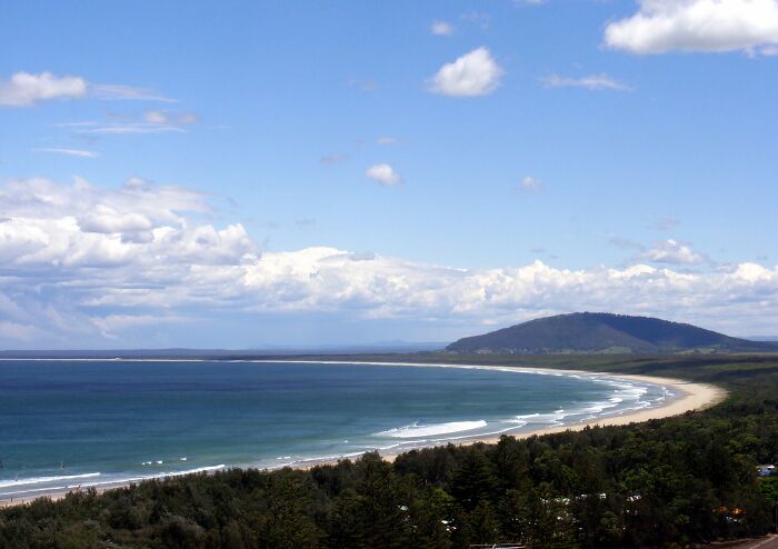 A stunning beach with clear blue waters and a scenic coastline under a partly cloudy sky.