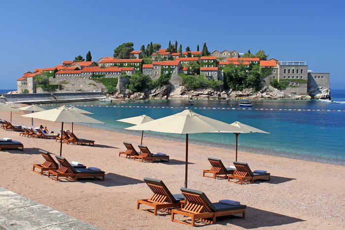 Stunning beach with loungers and umbrellas facing a historic coastal village.