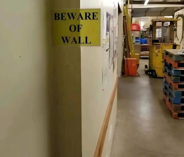Sign saying "Beware of Wall" in a corridor, highlighting unusual warning signs.