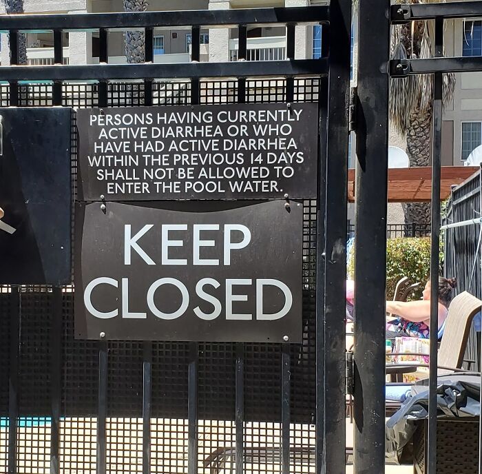 "Warning signs on pool gate advising against entry after diarrhea, with 'Keep Closed' message displayed prominently."