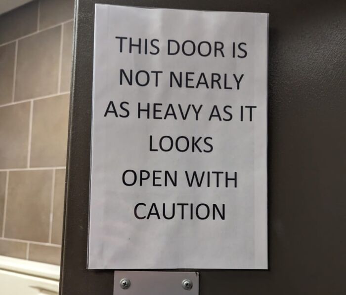 Sign on a door reading, "This door is not nearly as heavy as it looks. Open with caution." Warning signs.
