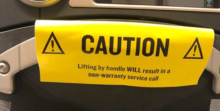 Caution sign on a machine, warning of non-warranty service call if handle is lifted, hinting at a big mistake.