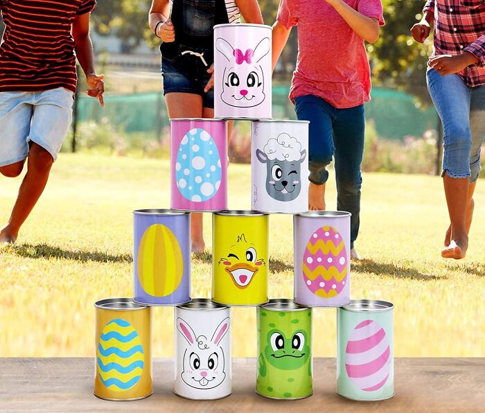 Children playing tin stack game with colorful Easter-themed cans outdoors.