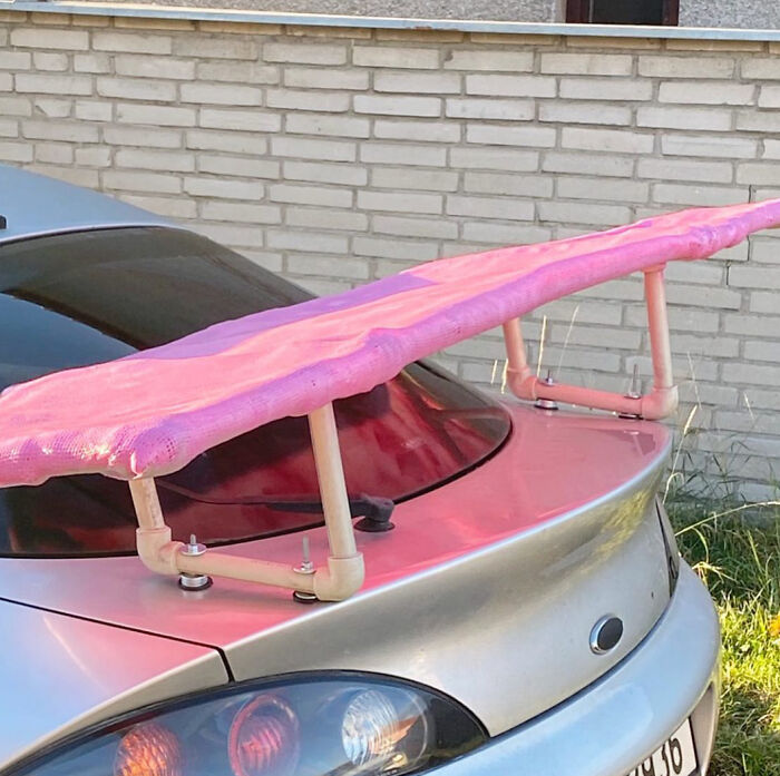 Car repair fail with a pink ironing board used as a spoiler on a silver vehicle.