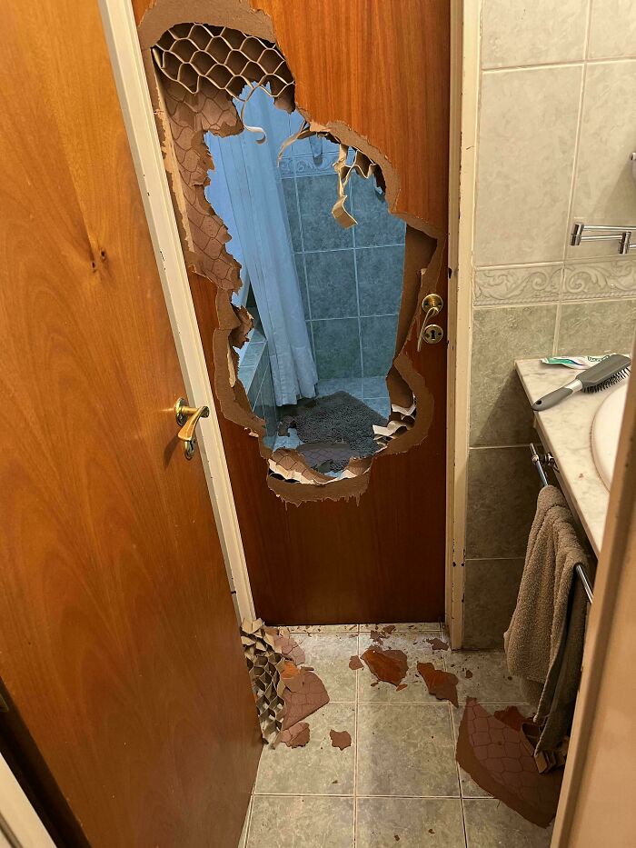 Damaged bathroom door with large hole and scattered debris, illustrating a horrible day.
