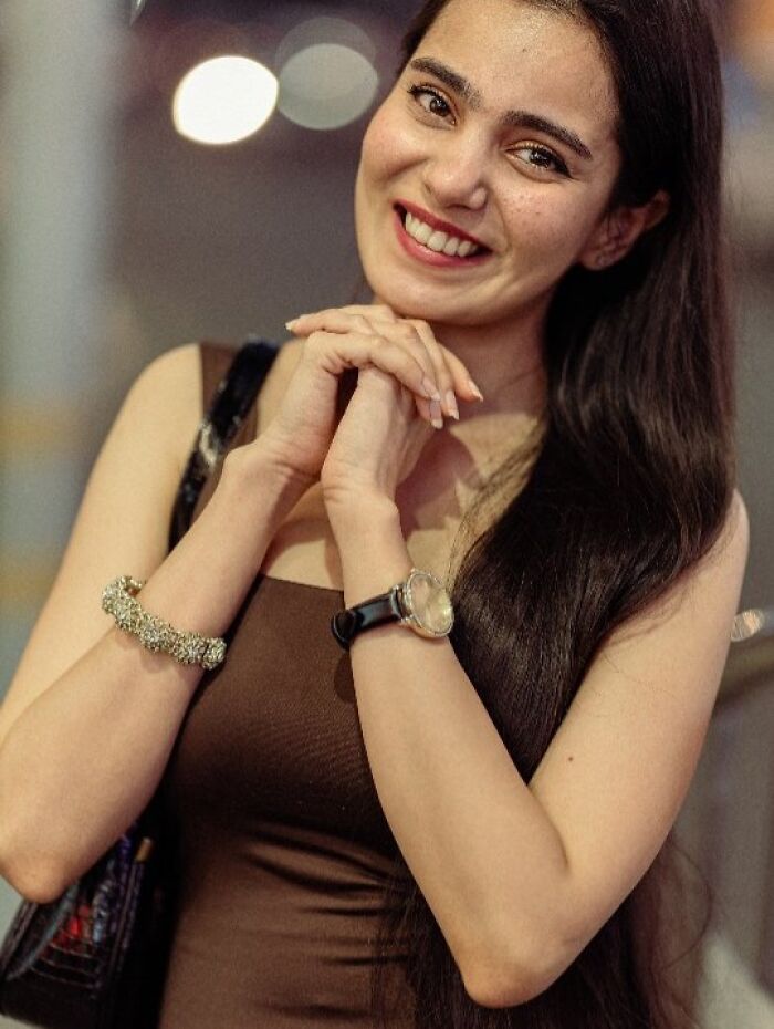 A woman smiles with hands clasped, captured in a stunning portrait by an Indian photographer.