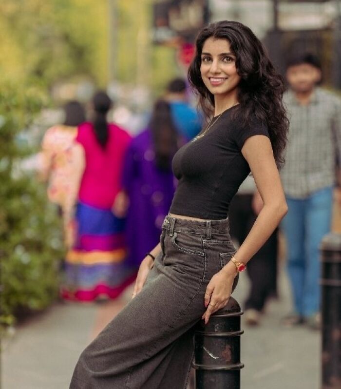 Portrait of a smiling woman in a black t-shirt, standing on a street, capturing the beauty of strangers through photography.