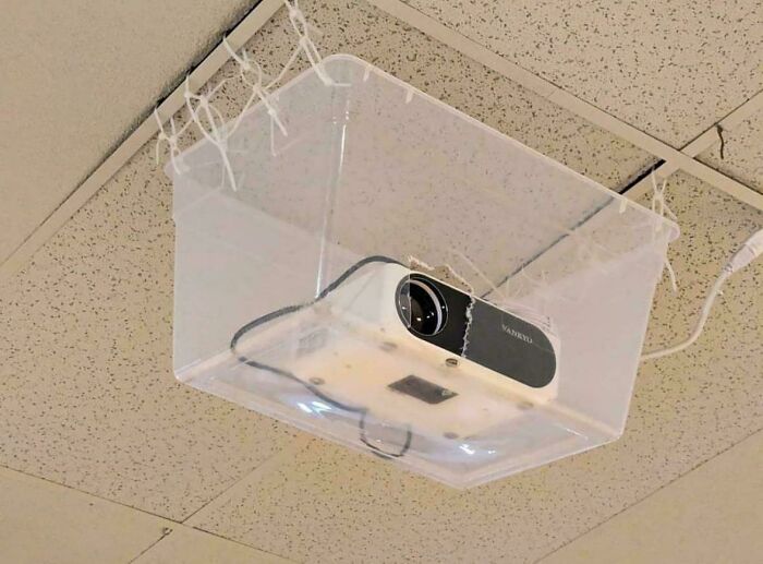 Projector in a plastic container on ceiling, highlighting repair failure.
