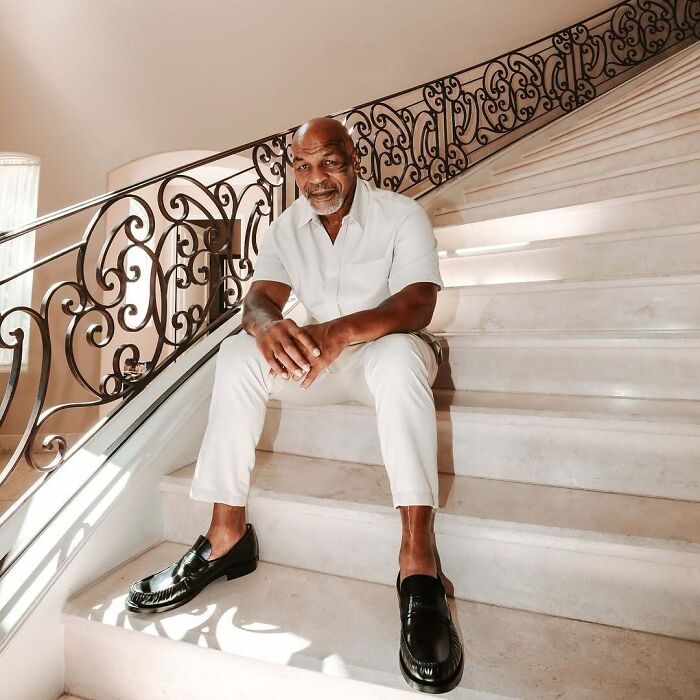 Man in white outfit sitting on ornate staircase, exemplifying celebrity lifestyle.