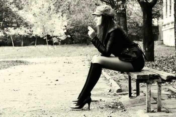 A woman in the 1960s sitting on a bench, wearing a hat and high heels, capturing the style of the JFK era in America.