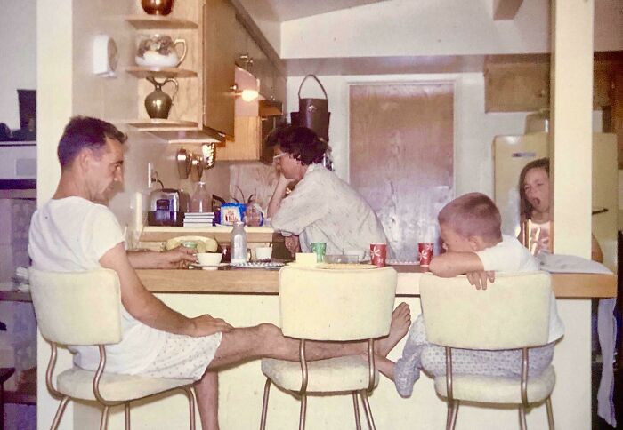 Family in a 1960s American kitchen during JFK era, sitting around a counter with vintage decor and casual attire.