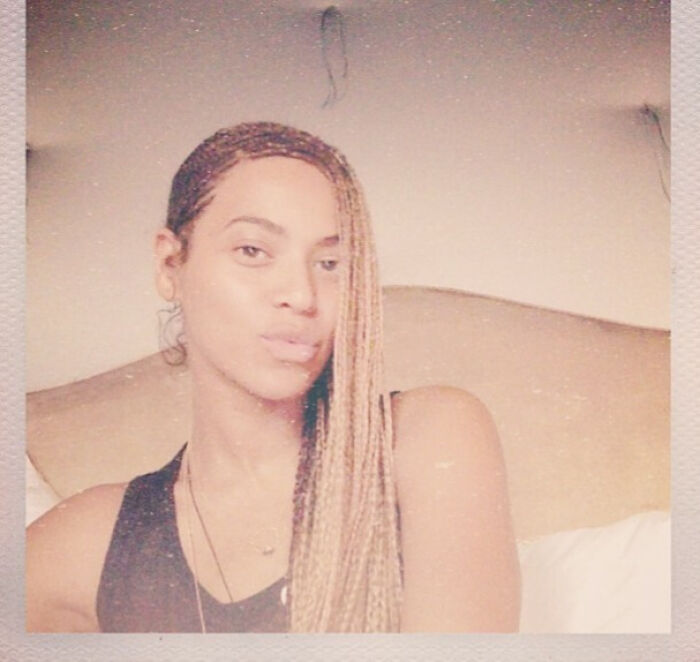 A woman with braids and a serious expression in a dimly lit room, capturing a moment of celebrity poise.